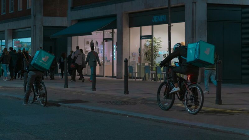 夜の街を自転車で走るDeliverooのフードデリバリー配達員