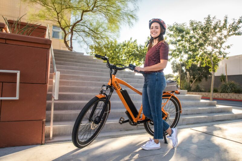 オレンジ色の海外モデル電動アシスト自転車とヘルメット姿の女性